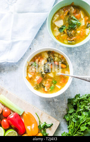 Minestrone, sur la Cuvette et pot de légumes couper sur une cutboard tomate cerise, citron vert, brun sur un fond blanc en béton Banque D'Images