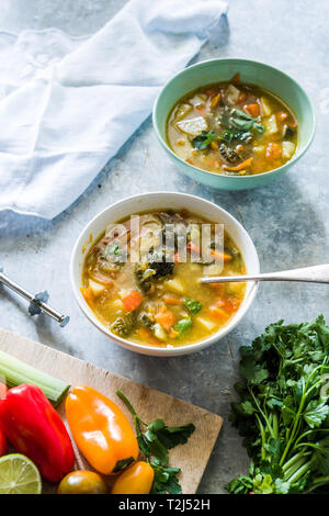 Minestrone, sur la Cuvette et pot de légumes couper sur une cutboard tomate cerise, citron vert, brun sur un fond blanc en béton Banque D'Images