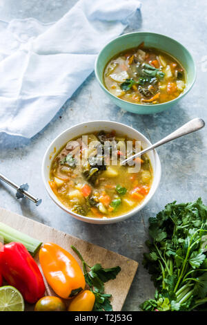 Minestrone, sur la Cuvette et pot de légumes couper sur une cutboard tomate cerise, citron vert, brun sur un fond blanc en béton Banque D'Images