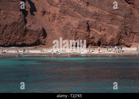 Vue sur les touristes se détendant sur une plage de Red Rock à Santorin depuis une croisière au coucher du soleil. Banque D'Images