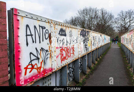 La peinture en aérosol graffiti sur un ancien chemin de fer rouille passerelle sur un sentier à Woking, Surrey, au sud-est de l'Angleterre, Royaume-Uni Banque D'Images