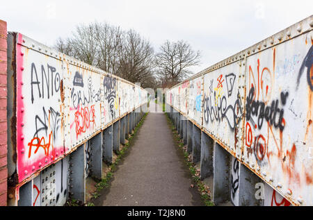 La peinture en aérosol graffiti sur un ancien chemin de fer rouille passerelle sur un sentier à Woking, Surrey, au sud-est de l'Angleterre, Royaume-Uni Banque D'Images