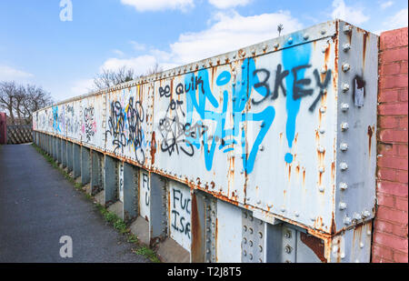 La peinture en aérosol graffiti sur un ancien chemin de fer rouille passerelle sur un sentier à Woking, Surrey, au sud-est de l'Angleterre, Royaume-Uni Banque D'Images