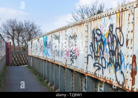 La peinture en aérosol graffiti sur un ancien chemin de fer rouille passerelle sur un sentier à Woking, Surrey, au sud-est de l'Angleterre, Royaume-Uni Banque D'Images