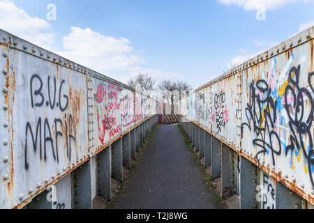 La peinture en aérosol graffiti sur un ancien chemin de fer rouille passerelle sur un sentier à Woking, Surrey, au sud-est de l'Angleterre, Royaume-Uni Banque D'Images