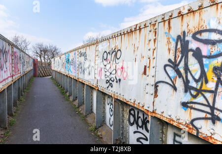 La peinture en aérosol graffiti sur un ancien chemin de fer rouille passerelle sur un sentier à Woking, Surrey, au sud-est de l'Angleterre, Royaume-Uni Banque D'Images