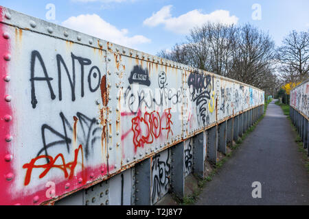 La peinture en aérosol graffiti sur un ancien chemin de fer rouille passerelle sur un sentier à Woking, Surrey, au sud-est de l'Angleterre, Royaume-Uni Banque D'Images