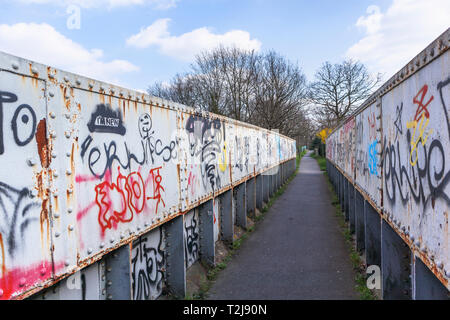 La peinture en aérosol graffiti sur un ancien chemin de fer rouille passerelle sur un sentier à Woking, Surrey, au sud-est de l'Angleterre, Royaume-Uni Banque D'Images