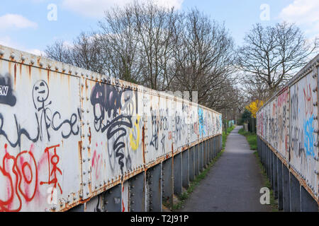 La peinture en aérosol graffiti sur un ancien chemin de fer rouille passerelle sur un sentier à Woking, Surrey, au sud-est de l'Angleterre, Royaume-Uni Banque D'Images