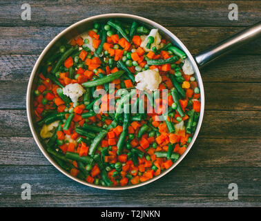 Lave la cuisine asiatique. Mélange de légumes des carottes, petits pois, haricots verts et chou-fleur dans une poêle sur une vieille table en bois, close-up vue supérieure. vitres teintées Banque D'Images