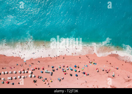 Bleu doux des vagues de la mer avec mousse blanche sur la plage de sable tropicale très tendance aux tons couleur corail vivant de l'année 2019 avec des parasols de drone. Banque D'Images