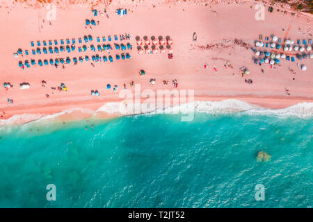 Bleu doux des vagues de la mer avec mousse blanche sur la plage de sable tropicale très tendance aux tons couleur corail vivant de l'année 2019 avec des parasols de drone. Banque D'Images