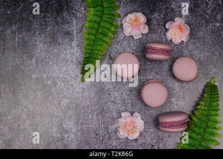 Macaron français cookies dessert rose lilas sur un fond noir avec des fleurs roses et vert feuille Banque D'Images