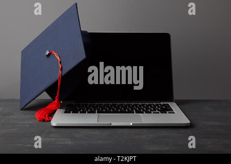 Ordinateur portable avec écran blanc et les universitaires avec gland rouge sur gris Banque D'Images