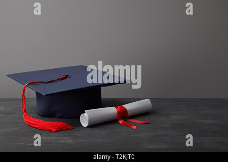 Diplôme universitaire et capuchon avec gland rouge sur la surface sombre sur gris Banque D'Images