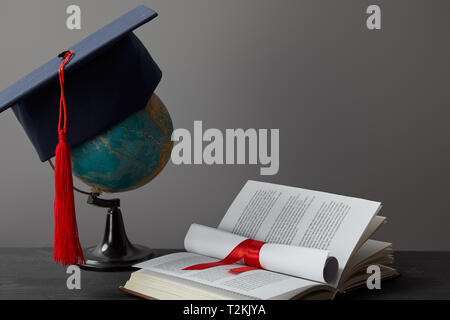 Globe, les universitaires, diplôme et livre ouvert sur gris Banque D'Images
