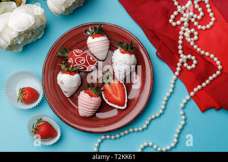 Une fraise mûre en glaçage au chocolat blanc se trouve sur une plaque bourgogne sur fond bleu turquoise Banque D'Images