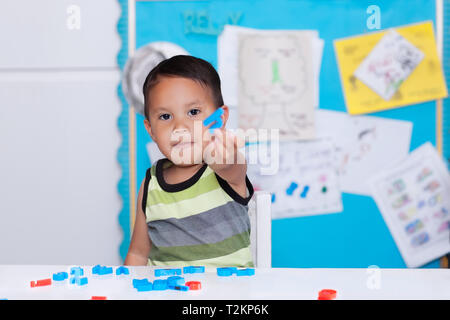 Garçon intelligent donnant ou en montrant un alphabet lettre en main, s'asseoir dans une salle de cours apprendre à épeler les mots et de démontrer ce qu'il a appris. Banque D'Images