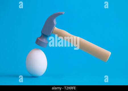 White egg et marteau en plastique jouet sur fond bleu pastel un minimum de concept créatif. Banque D'Images