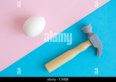Mise à plat d'oeufs blancs et un marteau en plastique jouet sur fond pastel un minimum de concept créatif. Banque D'Images