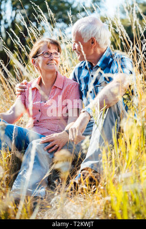 Couple de hauts femme et homme assis dans un pré dans l'herbe en regardant les uns les autres Banque D'Images