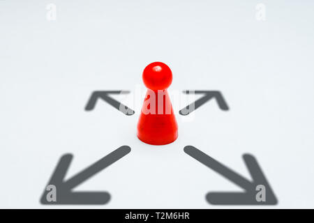 Un pion rouge pour les jeux au milieu de quatre flèches indiquant les directions isolé sur un fond uniforme blanc Banque D'Images