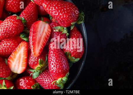 Fraises biologiques frais mûrs dans un bol sur fond noir. rustique Top View with copy space Banque D'Images