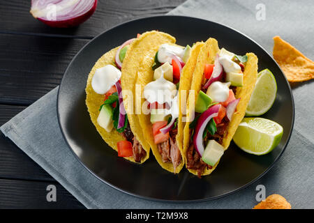 De délicieux tacos à coque dure servi avec des tranches de citron vert sur la plaque noire. Fillled tortilla croustillante avec du boeuf, de l'avocat, légumes et garni avec de la c Banque D'Images