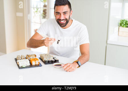 Handsome man smiling happy enjoying eating fresh sushi asiatique colorés à l'aide de baguettes Banque D'Images