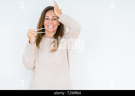 L'âge moyen femme tenant plus de baguettes asiatiques fond isolé a souligné avec la main sur la tête, choqué par la honte et la surprise face, en colère et frustra Banque D'Images