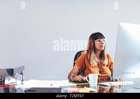 Illustrator assise à son bureau à l'office qui fait un dessin à l'aide d'un pavé numérique. Artiste Créateur travaillant sur ses dessins à l'ordinateur. Banque D'Images