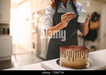 Chef pâtissier dans la cuisine Décorer un gâteau de chocolat. Femme en tablier pouring liquid sur un gâteau au chocolat sur comptoir de la cuisine. Banque D'Images