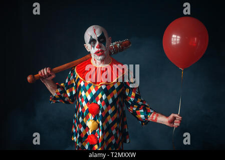 Clown sanglant laid avec batte de baseball et de l'air en montgolfière, l'horreur. Homme avec un miroir en costume de carnaval, crazy maniac Banque D'Images