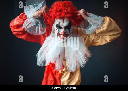 Scary clown sanglant larmes ses cheveux, secousse de colère. Homme avec un miroir en costume de carnaval, crazy maniac Banque D'Images