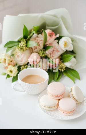 Ses macarons, dessert sucré élégante tasse de café et de couleur pastel beige fleurs bouquet sur gros plan de table blanc Banque D'Images