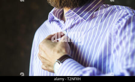 Gros plan du jeune homme barbu montre-bracelet en Boutonnant sa chemise rayée avant de partir. Porter au travail Concept. Banque D'Images