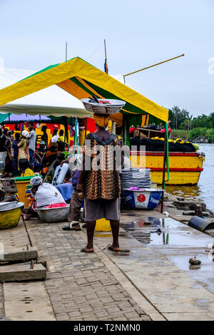 SEKONDI TAKORADI, GHANA - 10 avril 2018 : port dynamique scène du marché de la pêche en tant que femme en robe colorée porte rustique en métal godet sur sa tête prêt Banque D'Images