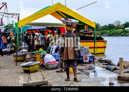 SEKONDI TAKORADI, GHANA - 10 avril 2018 : port dynamique scène du marché de la pêche en tant que femme en robe colorée porte panier sur sa tête prête à recueillir des pr Banque D'Images