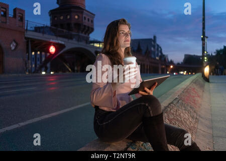 Jeune femme tenant une boisson chaude et à l'aide de tablette numérique sur pont, Berlin, Allemagne Banque D'Images