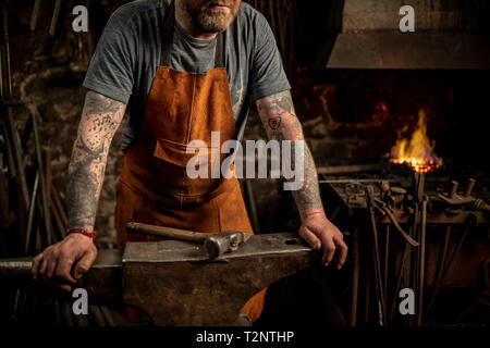 Mâle mature blacksmith appuyé contre anvil en atelier, cropped Banque D'Images