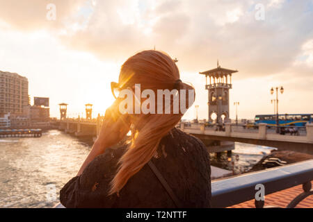 Woman with red hair faisant appel smartphone près de Stanley Bridge au coucher du soleil, vue arrière, Alexandria, Egypte Banque D'Images