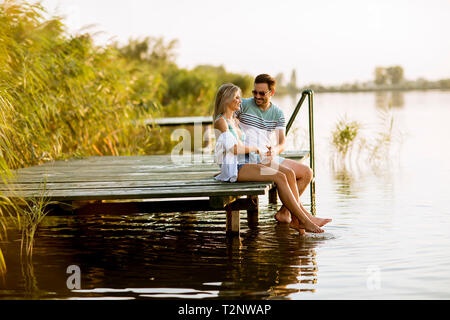 Couple d'amoureux assis sur la jetée sur le lac au coucher du soleil d'été Banque D'Images