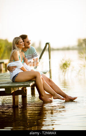 Couple d'amoureux assis sur la jetée sur le lac au coucher du soleil d'été Banque D'Images