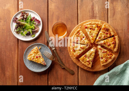 Une quiche fraîchement cuits au four avec du vin et de feuilles de salade mesclun, tourné par le haut sur un fond de bois rustique foncé with copy space Banque D'Images