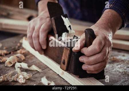 Mains d'un menuisier ébéniste, menuisier ou à l'aide d'un plan d'époque pour lisser la surface d'une planche de bois sur son workbench Banque D'Images