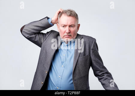 Pensive senior man in suit se gratte la tête ayant des doutes quant à son emploi. Banque D'Images