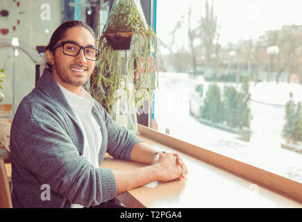 Adultes heureux homme barbu assis à table dans un café et smiling at camera. Closeup portrait of a handsome guy portant chemise blanche formelle,gray blou Banque D'Images