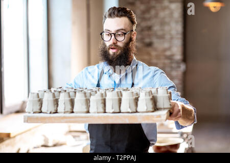 Portrait d'un beau barbu debout avec le bac plein de pièces en céramique à l'atelier de poterie Banque D'Images