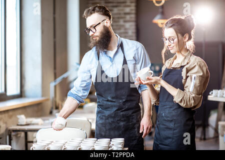 L'homme et la femme travaillant avec des pièces en argile produits céramiques sur le lieu de travail de l'atelier de poterie Banque D'Images