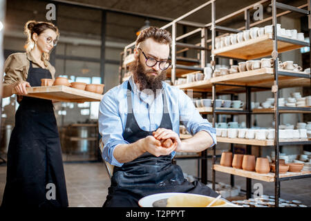Bel homme tablier en préparation de l'argile tout en rendant à sur la roue lors de la fabrication de poterie Banque D'Images